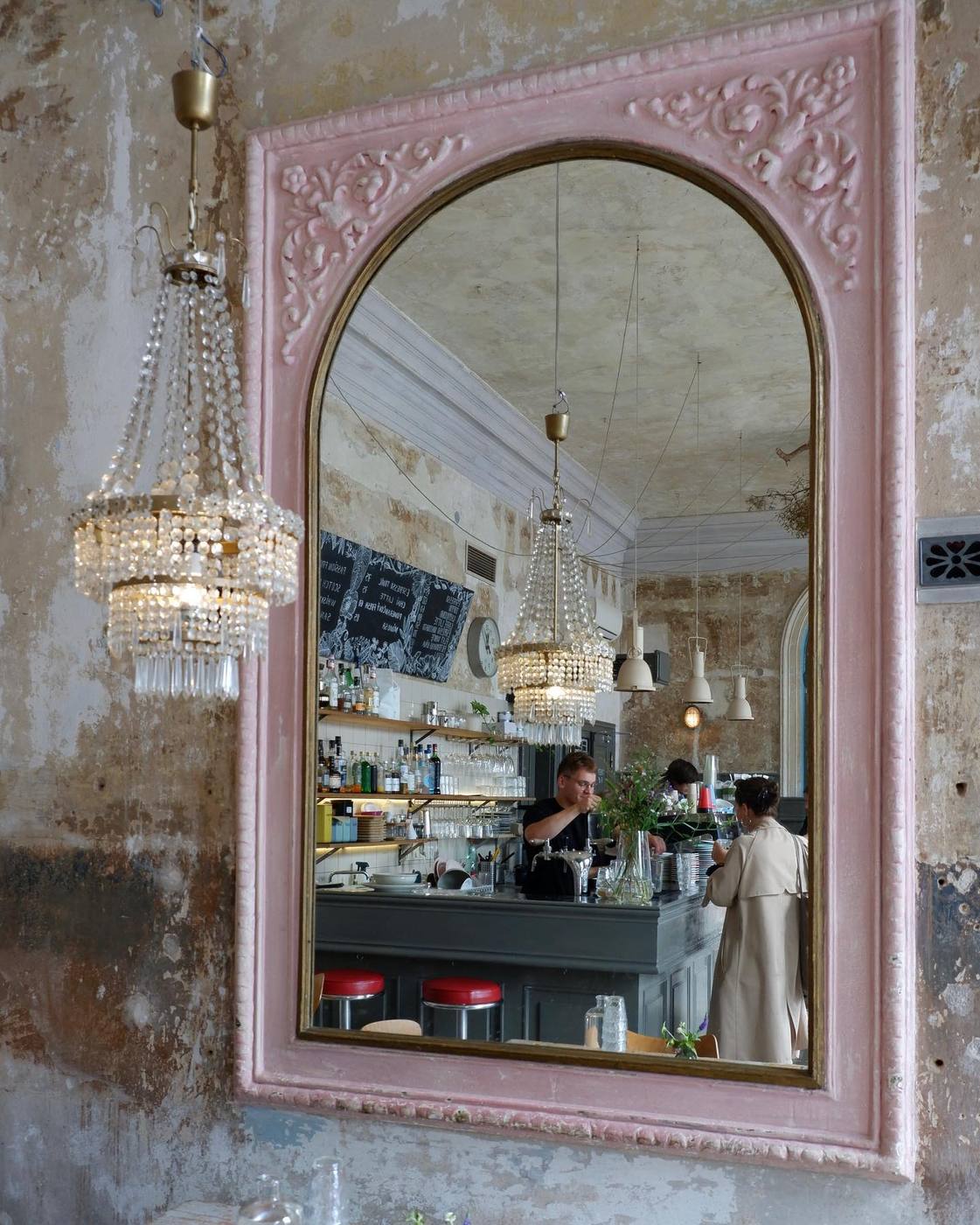 Pink-framed mirror reflecting chandeliers and the coffee bar at Café Letka