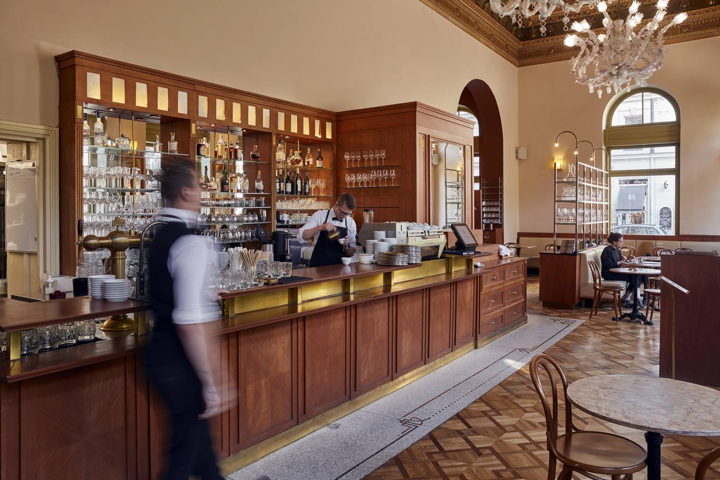 A waiter passing the long wooden bar under the painted ceiling