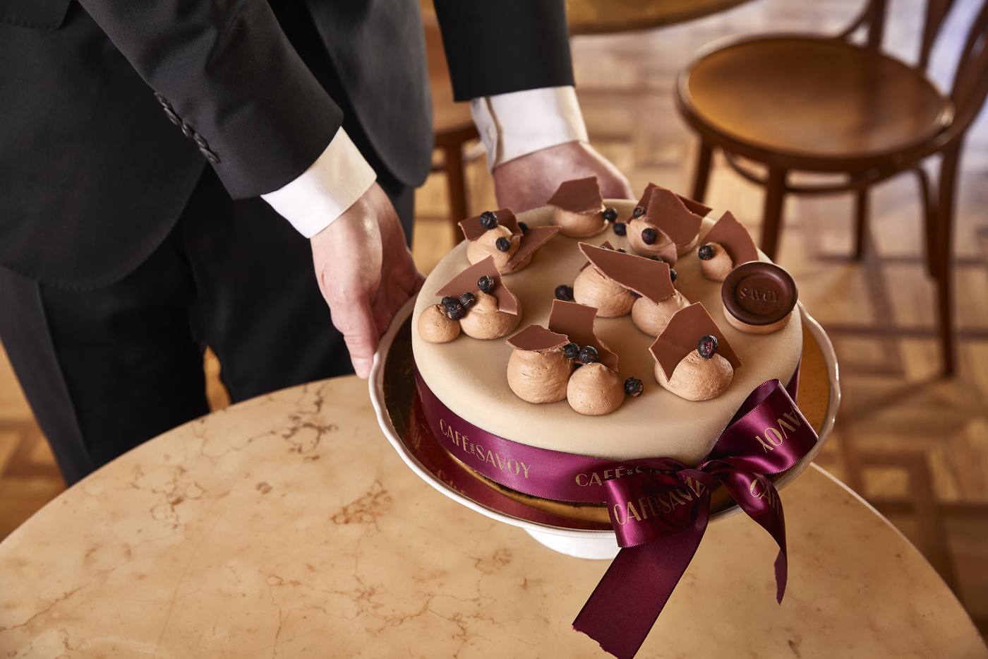 A waiter presenting the chocolate Savoy cake tied with a purple ribbon