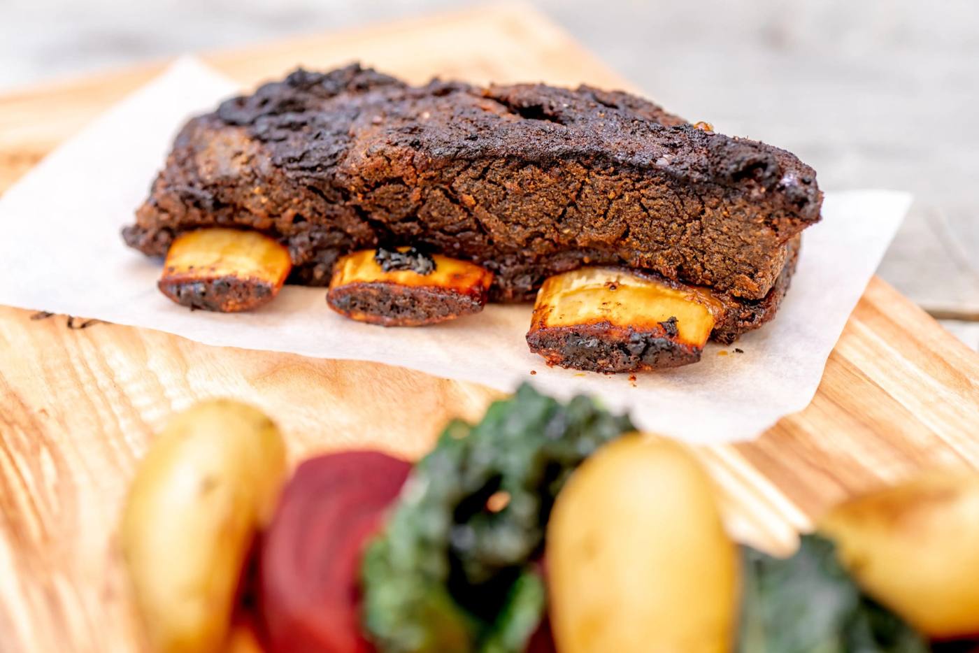 Smoked beef rib with potatoes, beetroot and greens on a wooden board
