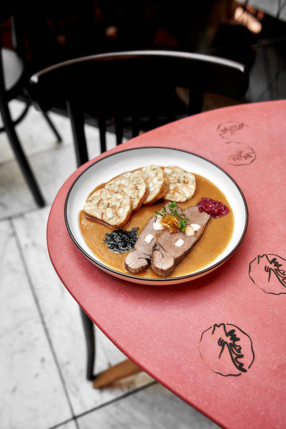 Venison svíčková with bread dumplings and cranberries on a red table