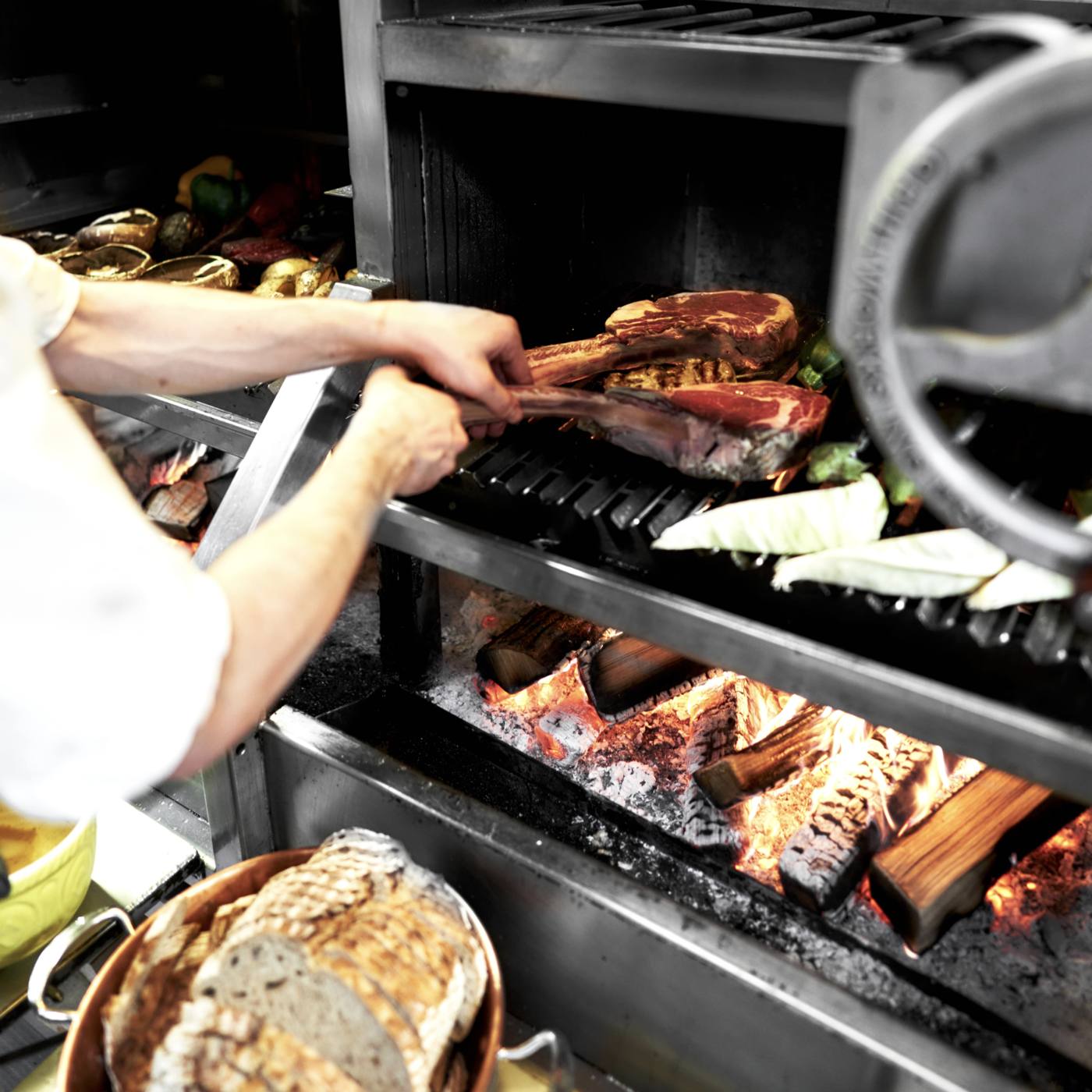 Steaks and bread cooking over wood fire on the Infierno grill