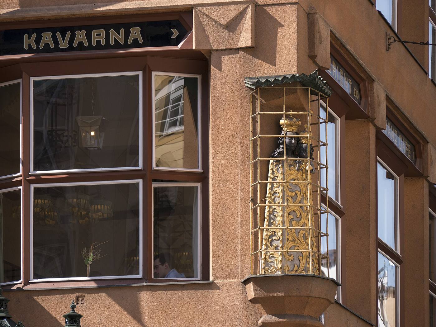 The Black Madonna statue in a gilded cage on the corner of the house, next to the Kavárna sign
