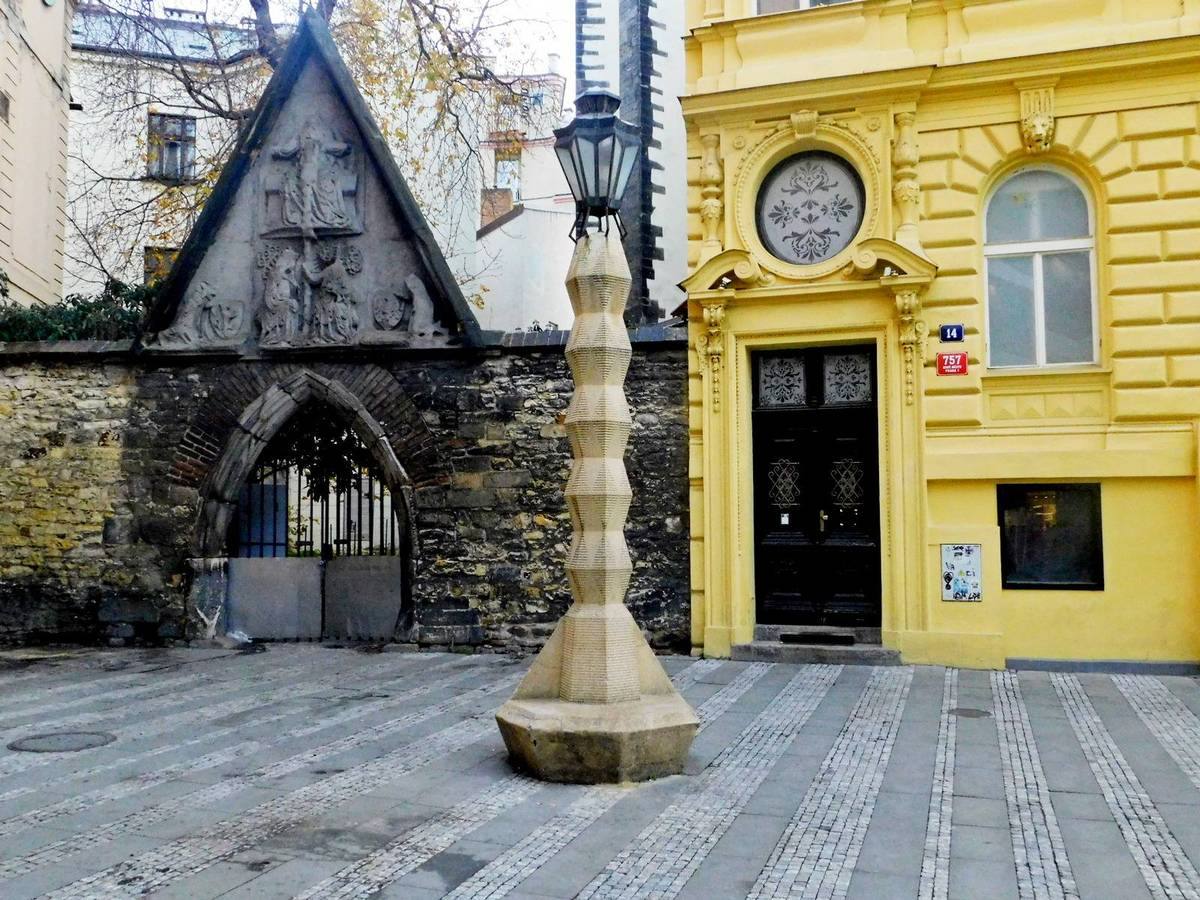 The faceted cubist stone lamppost on Jungmannovo náměstí in front of a Gothic gateway