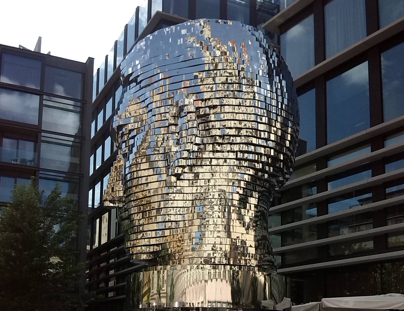 Close view of the layered stainless-steel Kafka head reflecting the surrounding glass facades