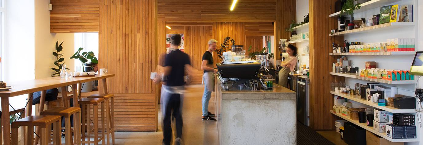 Baristas at work behind a concrete coffee bar with wood-panelled walls and retail shelves