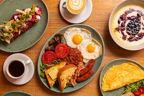 Breakfast spread with a full English plate, omelette, porridge and coffees