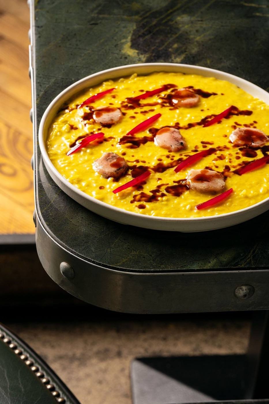 A saffron-yellow dish finished with red sauce on a dark green marble table