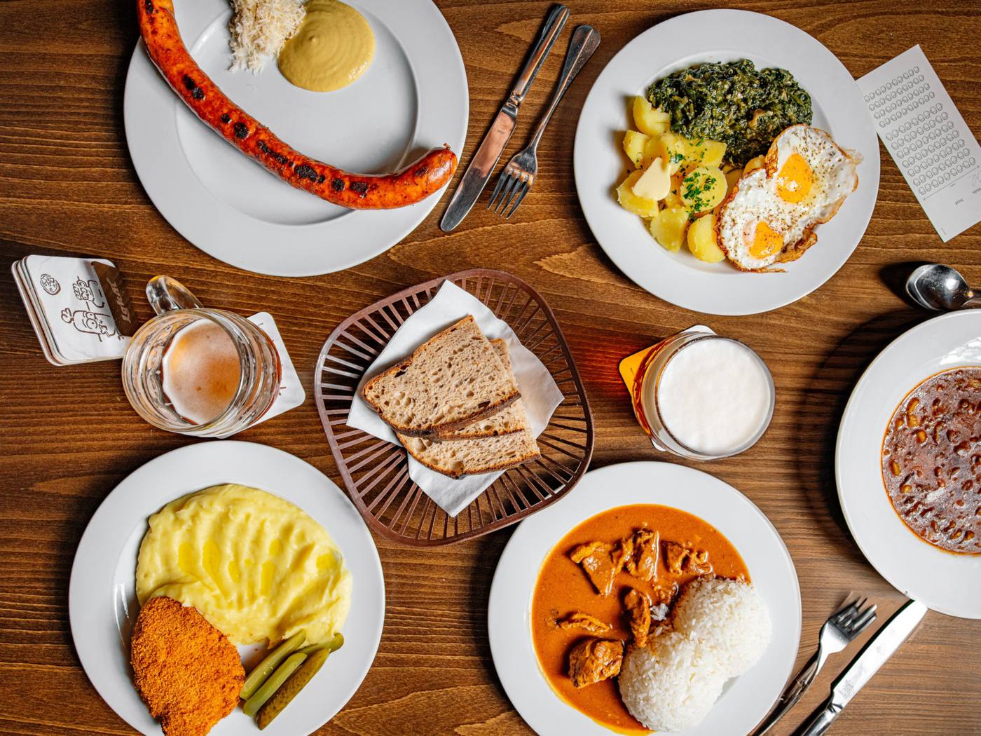 Table of Czech pub dishes: schnitzel, goulash, sausage, spinach with eggs and beer