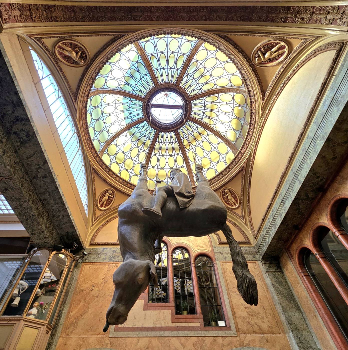 The horse sculpture hanging beneath the round stained-glass skylight of the Lucerna passage