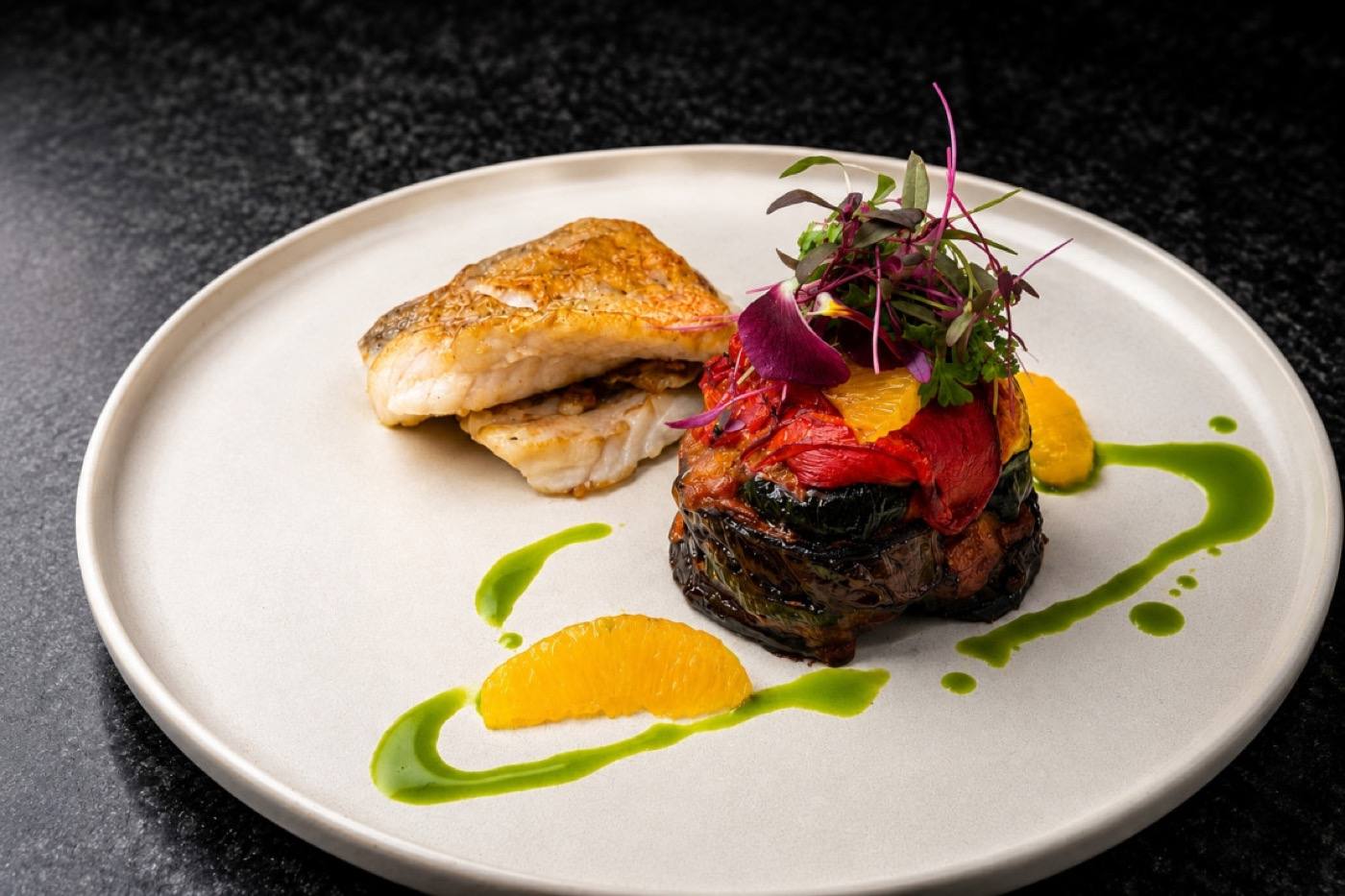 Crisp-skinned fish fillet with roasted tomato, microgreens and herb-oil dots