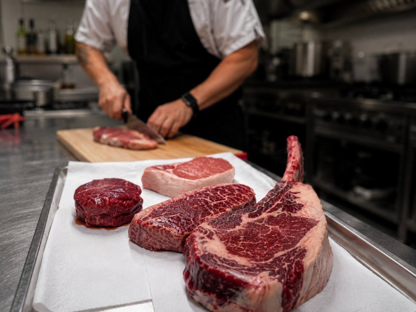 Chef portioning dry-aged steaks, including a tomahawk, in the kitchen