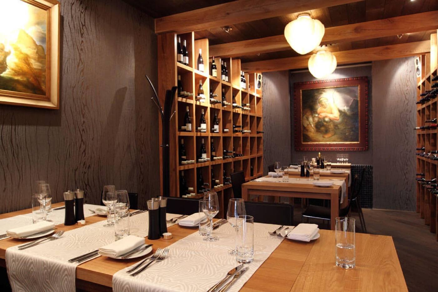 Warm-lit dining room with oak tables, wine racks and oil paintings on the walls