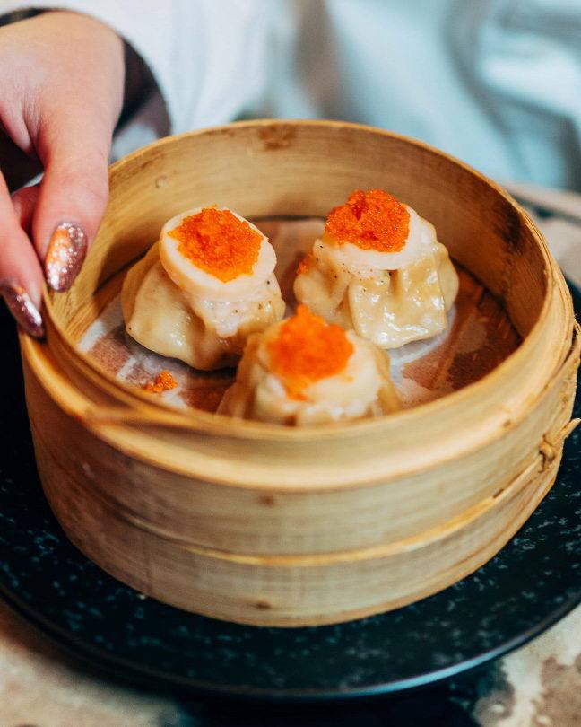 Bamboo steamer of shumai dumplings topped with orange roe