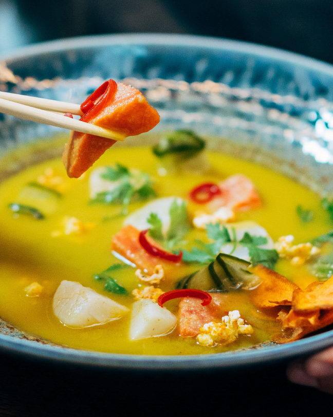 Bowl of seafood in bright yellow curry, lifted with chopsticks