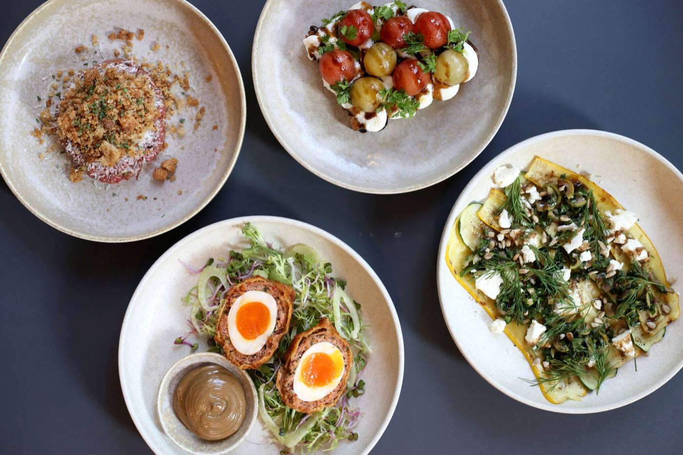 Four small plates seen from above, including Scotch eggs, tomatoes with mozzarella and a courgette salad