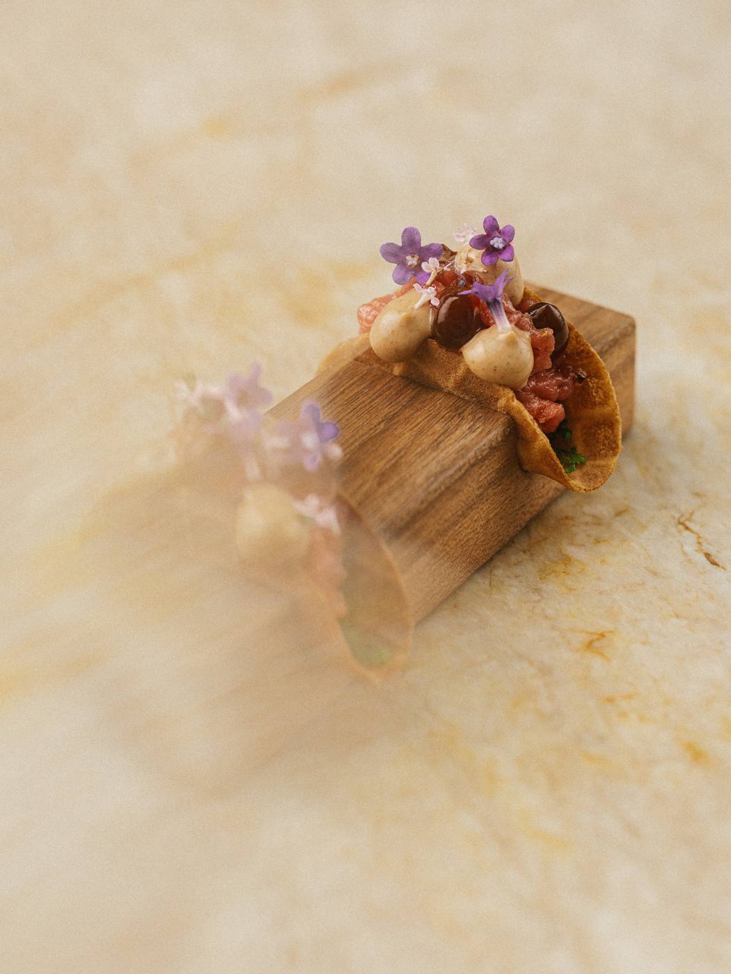 A small tasting-menu course with purple flowers served on a wooden block