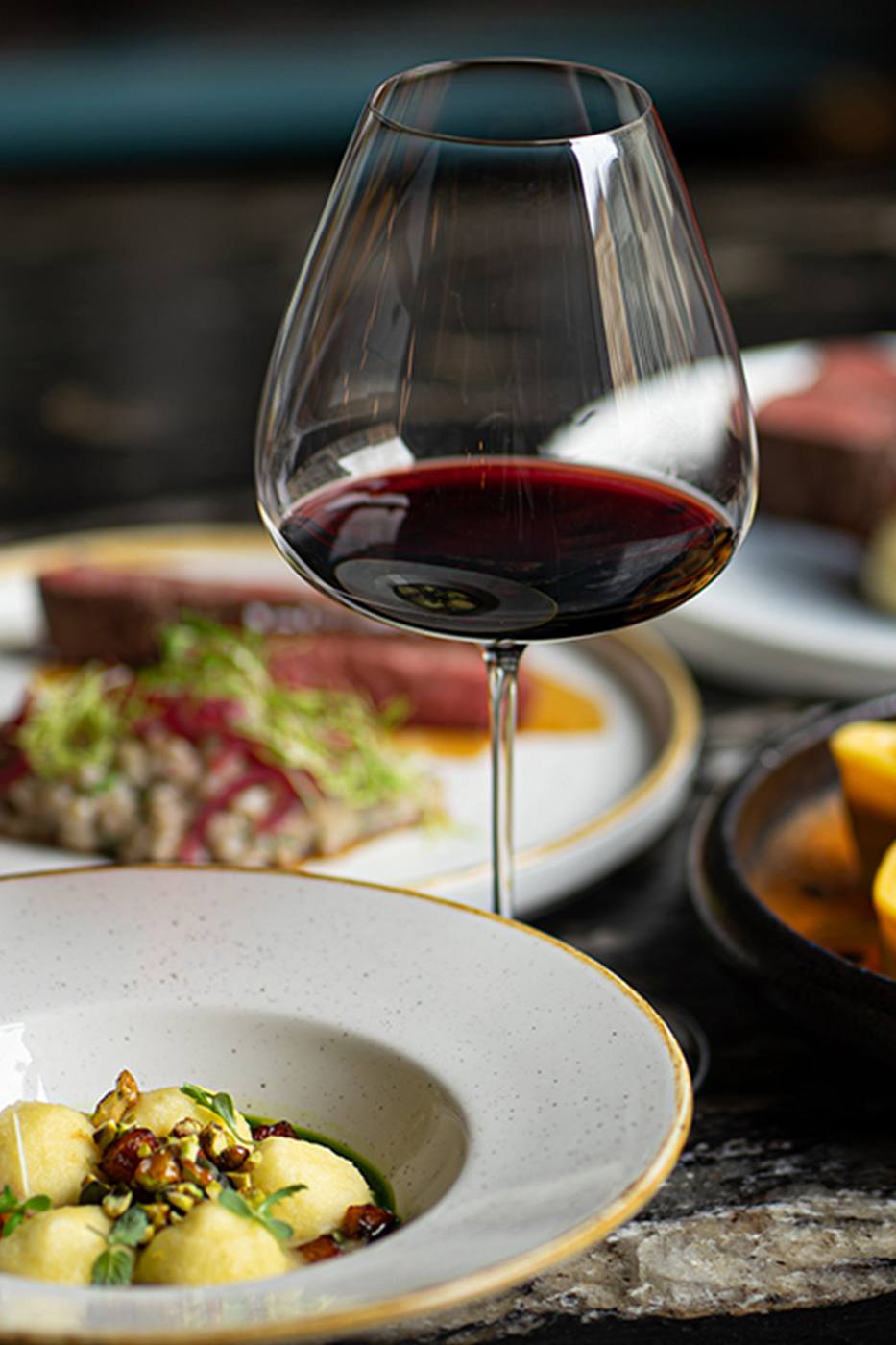 A glass of red wine among several small plates on a dark table