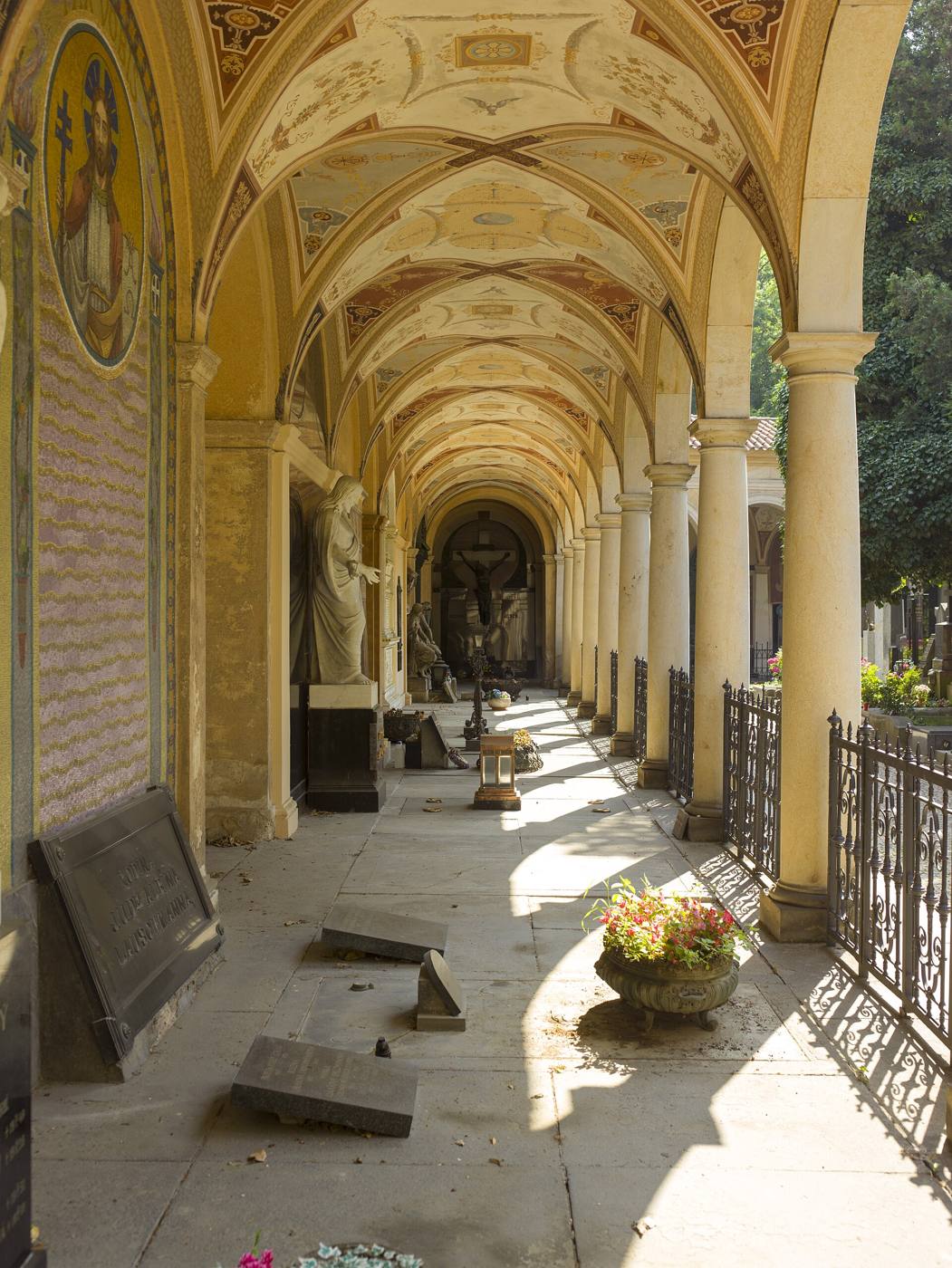 Painted vaulted arcade lined with tombstones and sculptures in Vyšehrad Cemetery